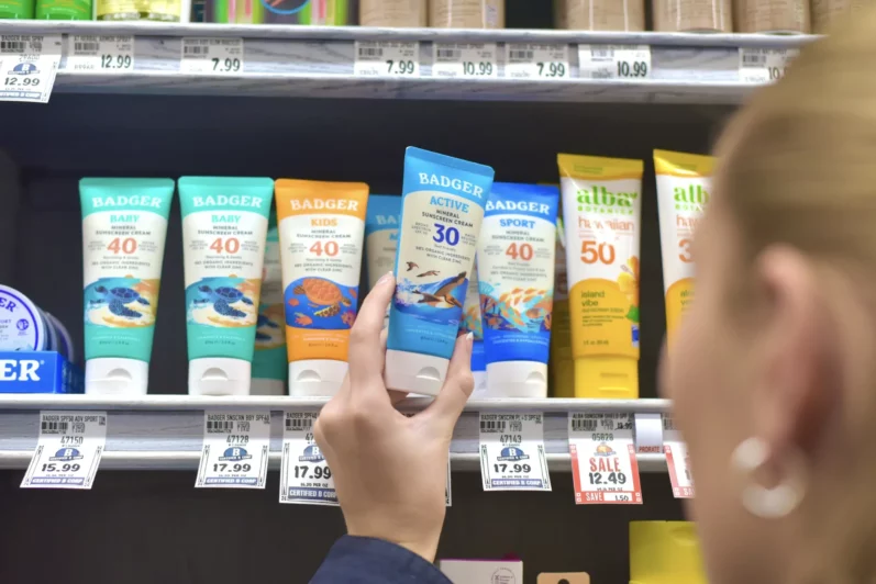 A shopper examining a Badger sunscreen on a natural products store shelf.